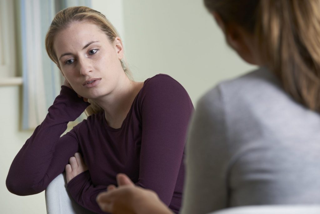 A young white woman sitting in a white chair during a counselling session.