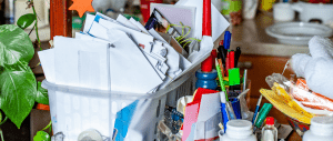 A messy kitchen countertop with a plastic bin overflowing with papers and other objects