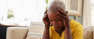A black older adult holding her head in her hands looking stressed