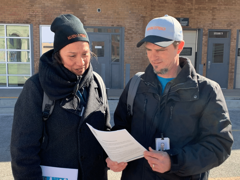 Deux membres du personnel de SFWE, un homme et une femme, debout l’un à côté de l’autre devant un édifice